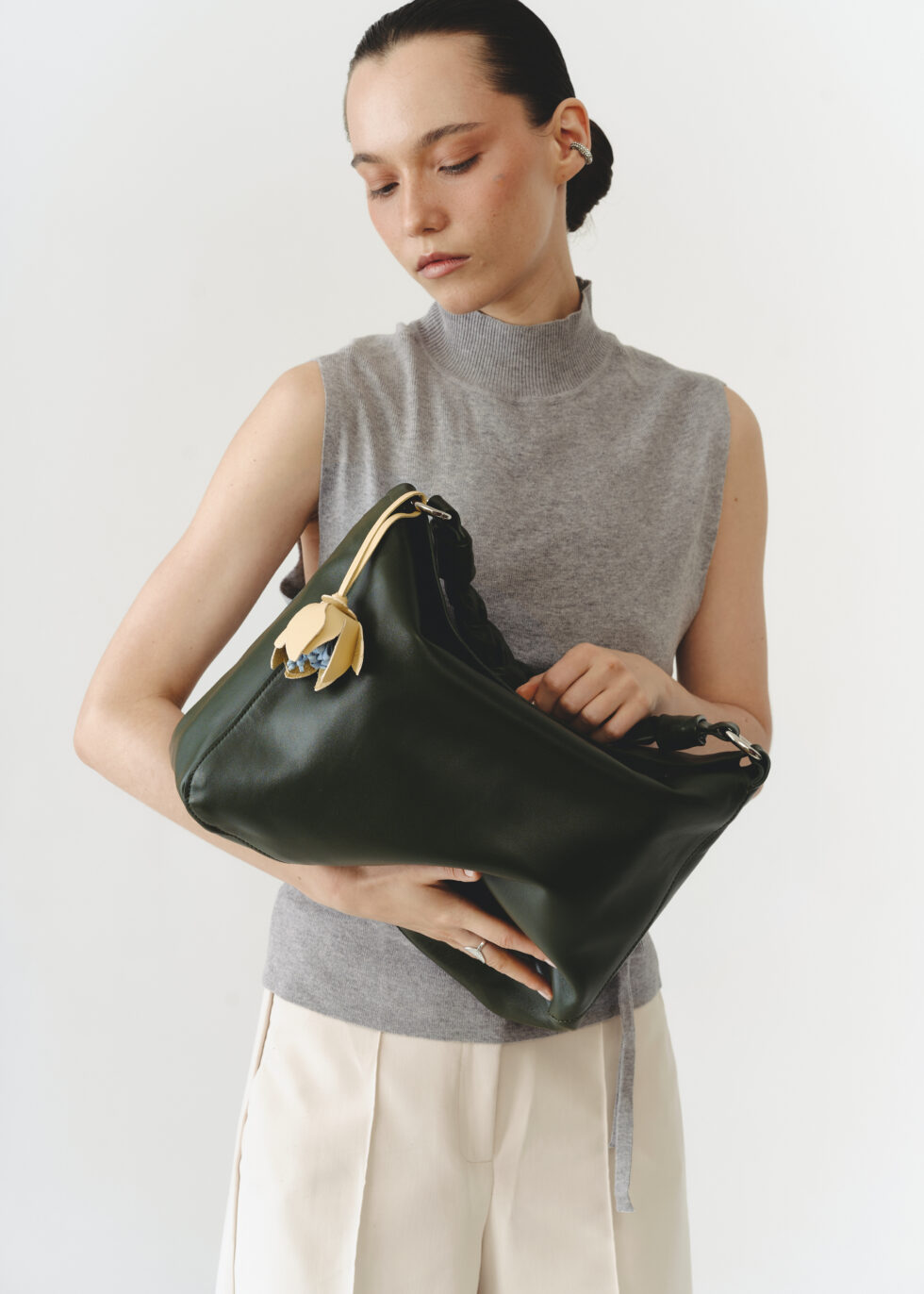 сумка хобо хакі з квіткою-підвісом в руках у моделі