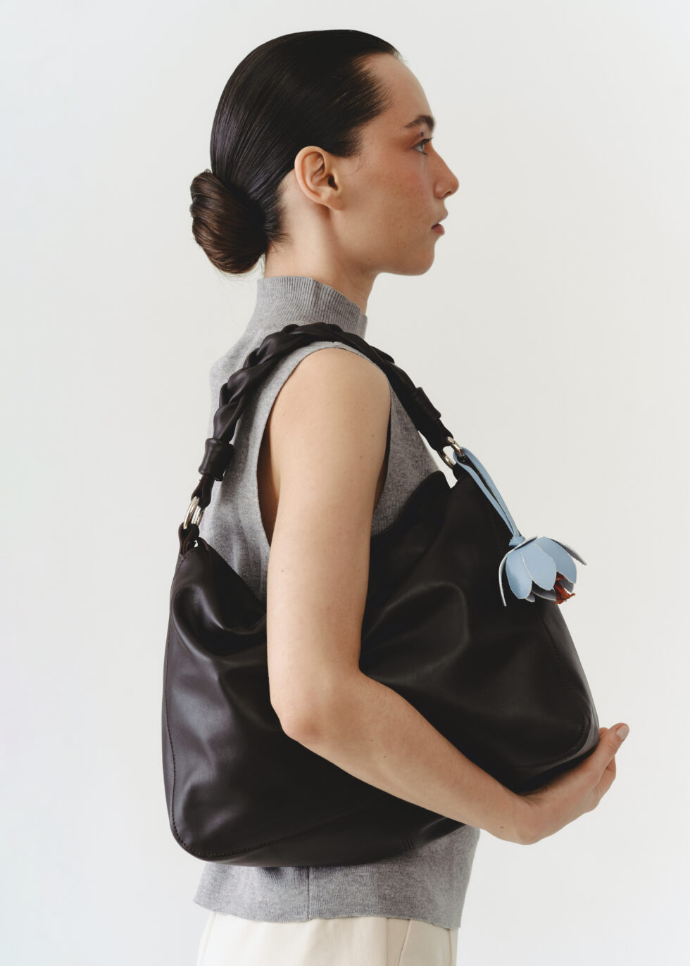 коричнева сумка хобо на плечі у моделі з квіткою-підвісом